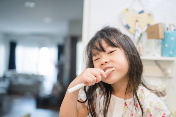 Little girl smiles as she brushes her mouth with fluoride toothpaste.