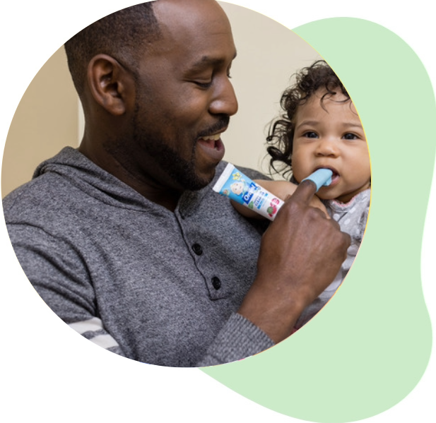 Dad uses Orajel Baby Tooth & Gum Cleanser with finger brush to brush infant's teeth.